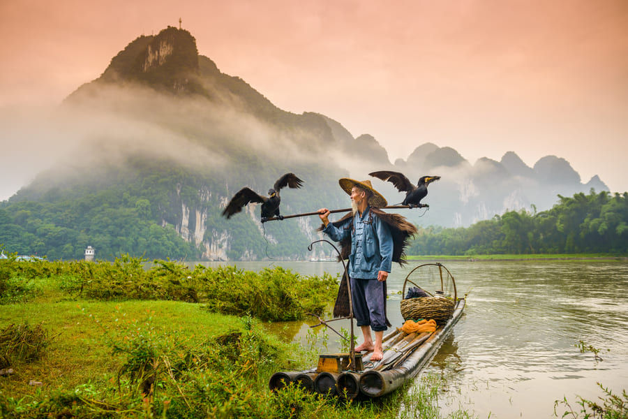 pescador de cormoran en atardecer bajo las montañas de china